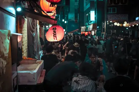 Friends gathered at a lively izakaya alley in Tokyo at night, red lanterns glowing overhead